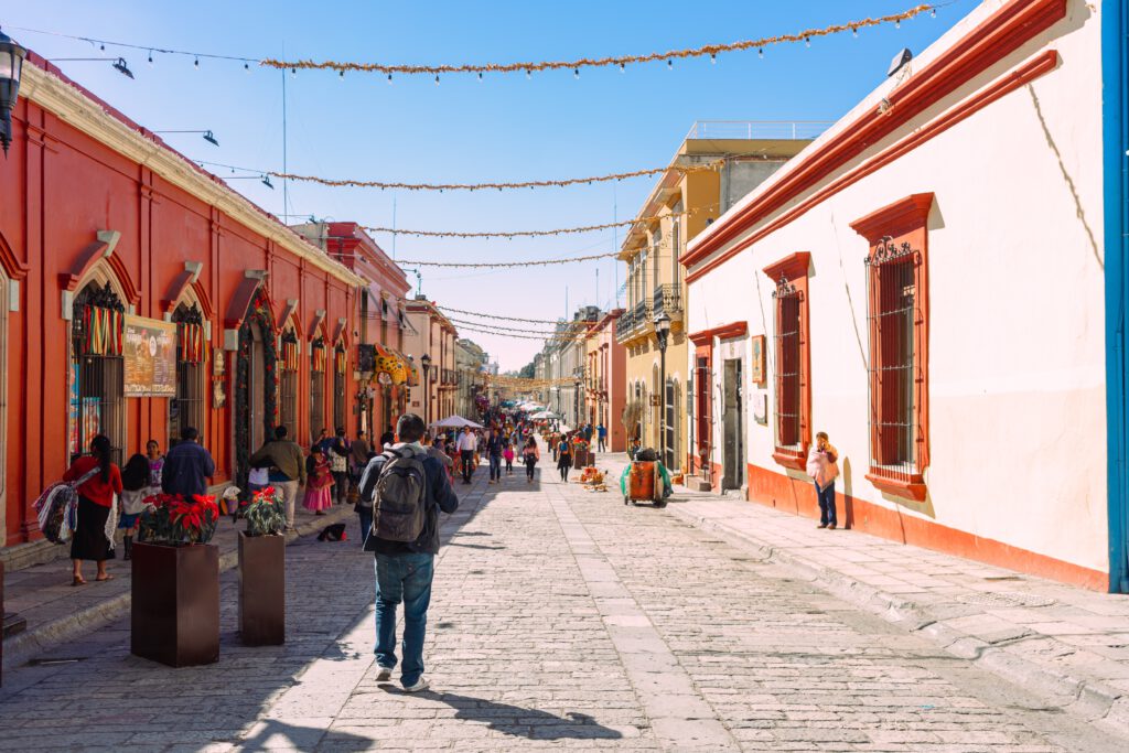 Picture of the streets of Oaxaca City with orange houses, and a man walking with his backpack