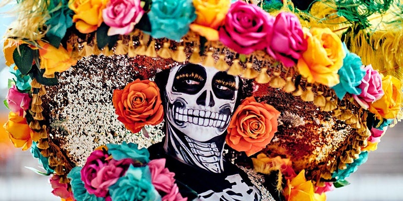 Person with painted skull face for day of the dead, wearing a big hat with colorful flowers