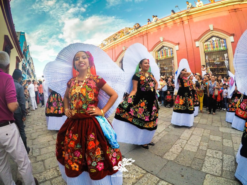 women in traditional dresses with flowers on the street in Oaxaca, orange house behind