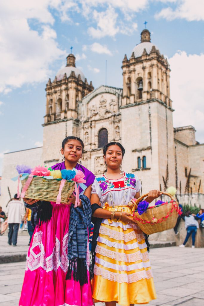 Oaxacan girls in colorful dresses on the main sqaure Zocalo, holding baskets