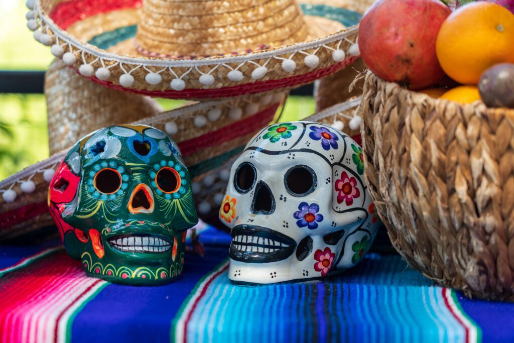 painted Mexican skull ceramics and two sombrero hats and a basket with fruits