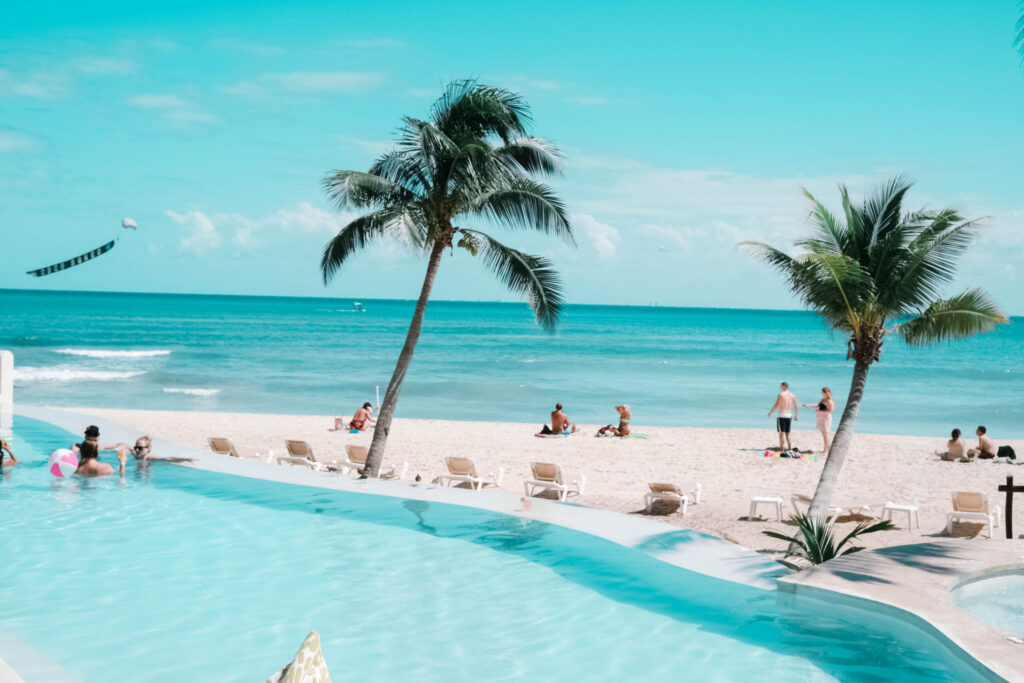 turquoise water pool leading to a turquoise water ocean on the beach in playa del Carmen, next to two palm trees