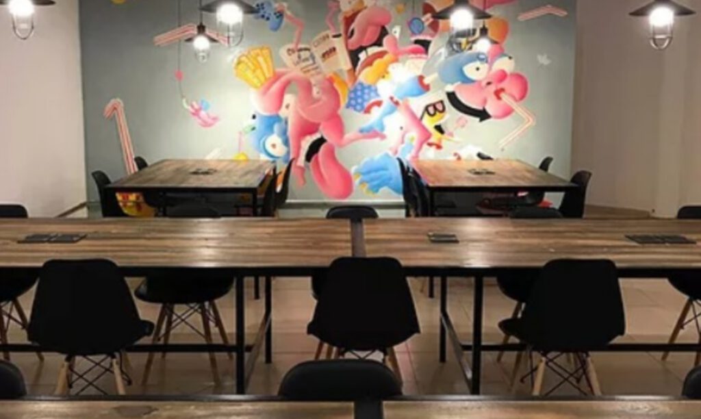 co-working space with long tables and several chairs., and a mural painting in the back
