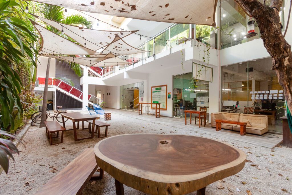 round wooden table outdoors, surrounded by trees, on a yard next to a building with office spaces, no people