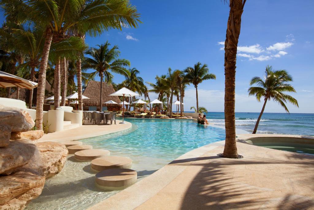 pool surrounded by palm tress in round shape, with view to the ocean in turquoise color