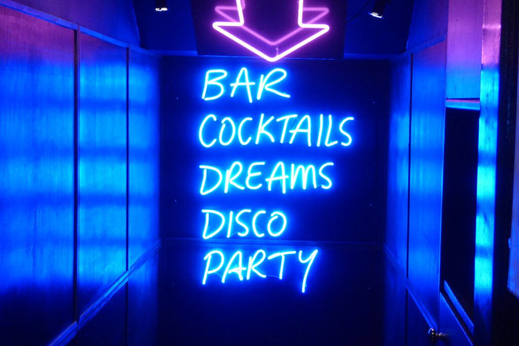 illuminated writing on a blue wall saying bar, cocktails, dreams, disco, party