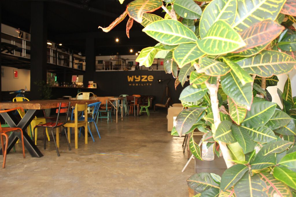 big co-working space with wooden tables and colorful chairs, also plants, black walls