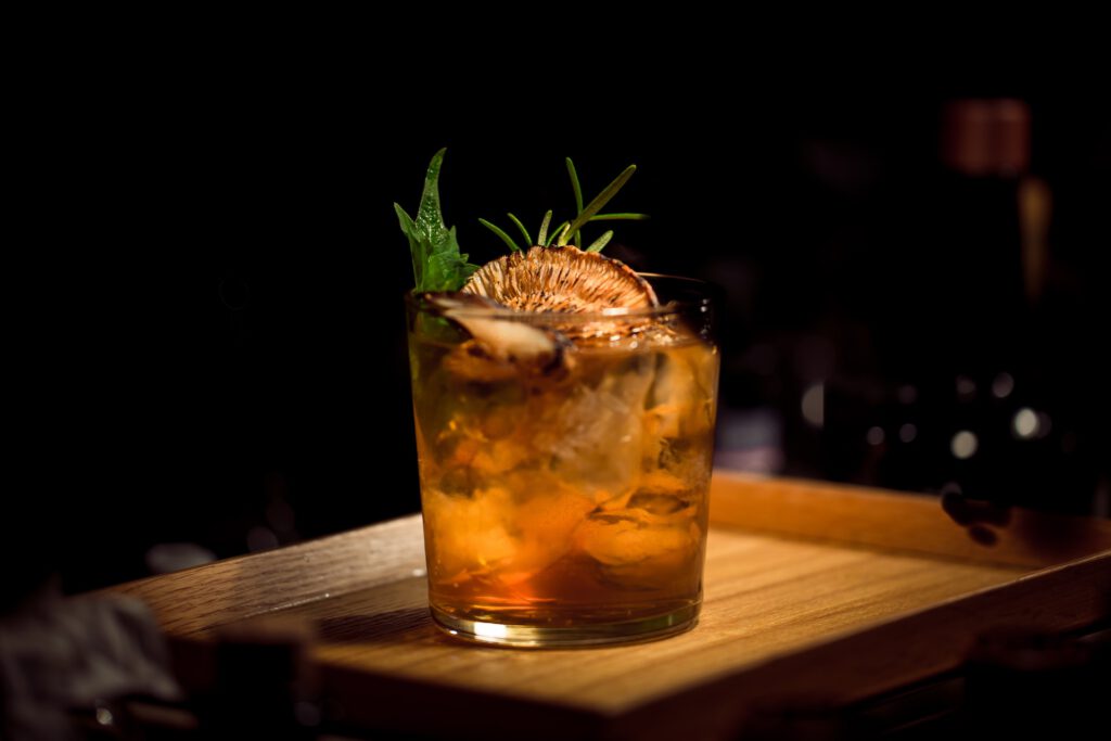 brown cocktail in a glass with herbs and dried orange piece